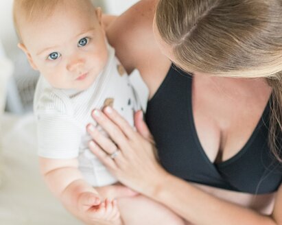 A baby looks into the camera above while being held by its mom.