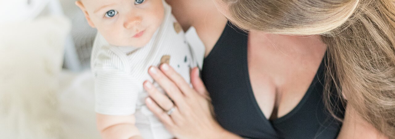 A baby looks into the camera above while being held by its mom.