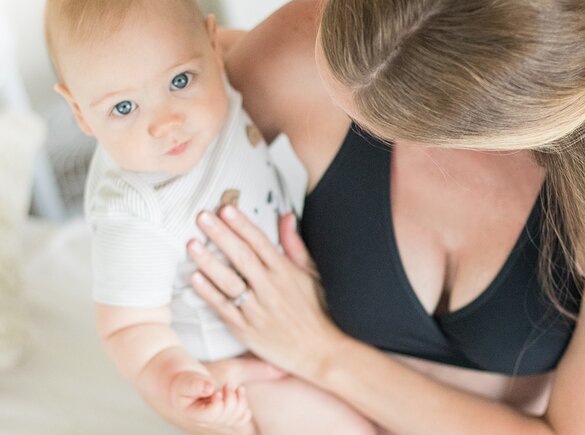 Een baby kijkt in de camera terwijl hij door zijn moeder wordt vastgehouden.