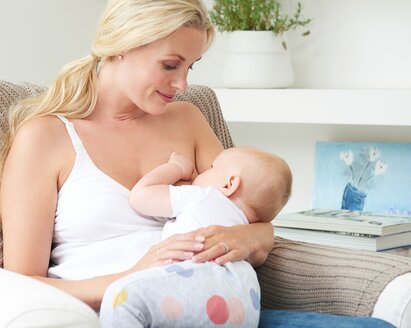 Una madre è seduta sulla sedia di casa e allatta il suo bambino.