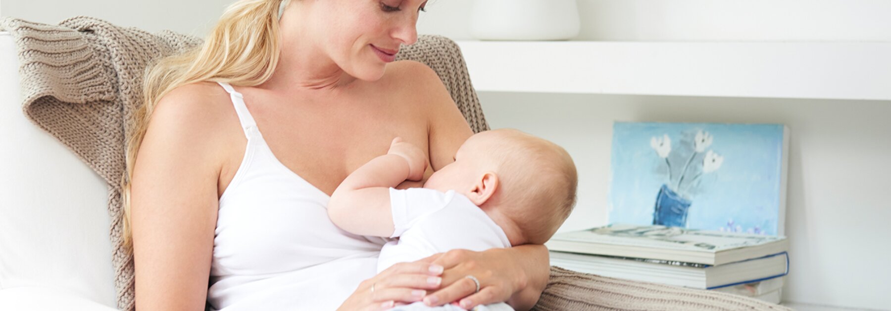 Een moeder zit thuis op de stoel en geeft haar baby borstvoeding.