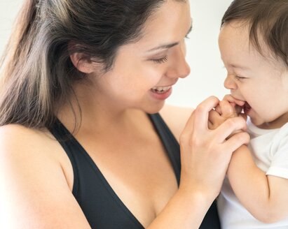 Un bambino cerca di mettersi le mani in bocca e la madre gliele stringe giocosamente, facendolo sorridere.