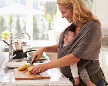 Una madre prepara un pasto sano per favorire una buona alimentazione durante l'allattamento, mentre il suo bambino dorme in una fascia attaccata a lei.