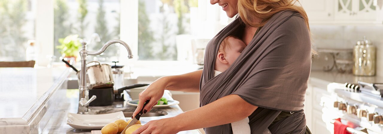Una madre prepara un pasto sano per favorire una buona alimentazione durante l'allattamento, mentre il suo bambino dorme in una fascia attaccata a lei.