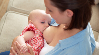 A mother is at home breastfeeding her baby.
