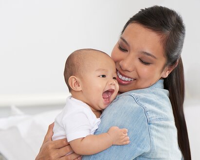 Una mamá sostiene a su bebé feliz y sonríe.