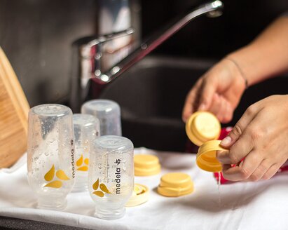 A mother washes Medela breast milk bottles and lays them on a towel to dry.