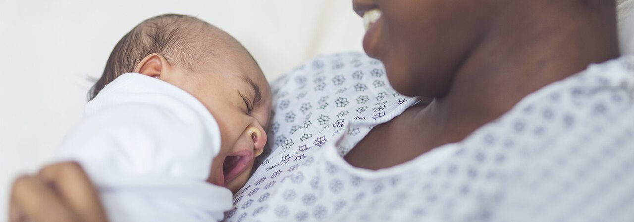 Una madre sonriente sentada en un hospital con su bebé recién nacido en el pecho.