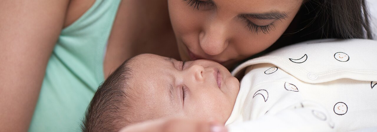Bebé tumbado en una cama y madre inclinada sobre el bebé y besándole la mejilla