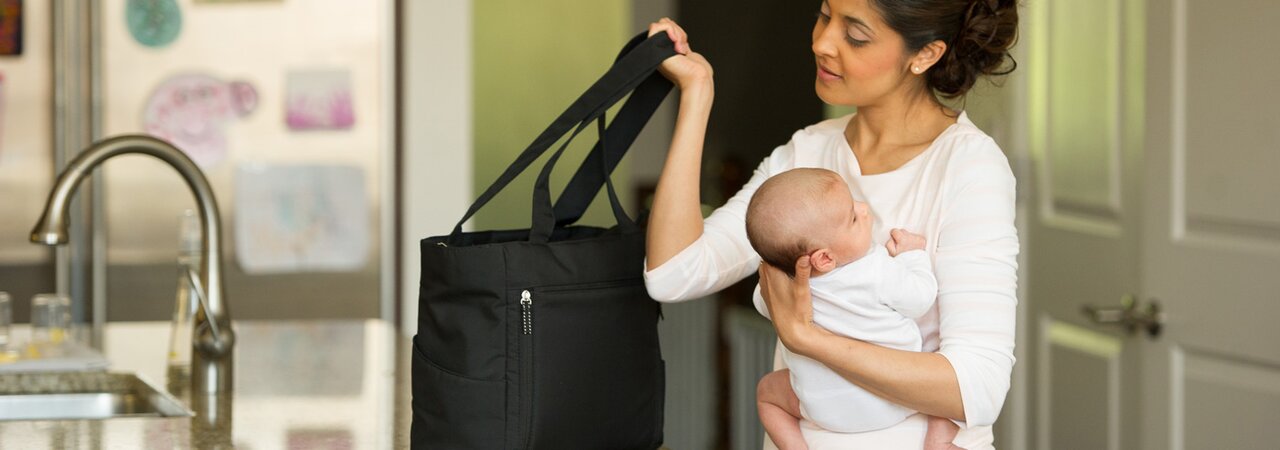 Una mamma che si prepara a uscire di casa tenendo in braccio il suo bambino in cucina.