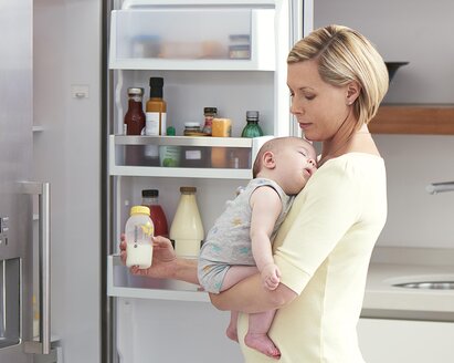 Een moeder houdt haar baby vast in de keuken terwijl ze gekoelde afgekolfde melk klaarmaakt voor een voeding.