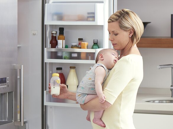 Een moeder houdt haar baby vast in de keuken terwijl ze gekoelde afgekolfde melk klaarmaakt voor een voeding.