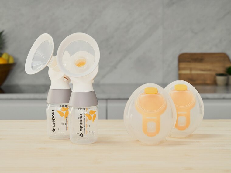 Ein Set von Medela Hands-free Collection Cups mit einem Medela classic PersonalFit Flex™ Doppelabpumpset, Schläuche nicht abgebildet, auf einer Theke sitzend.