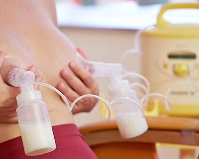 Woman sitting in a chair double pumping using a Medela Symphony breast pump.