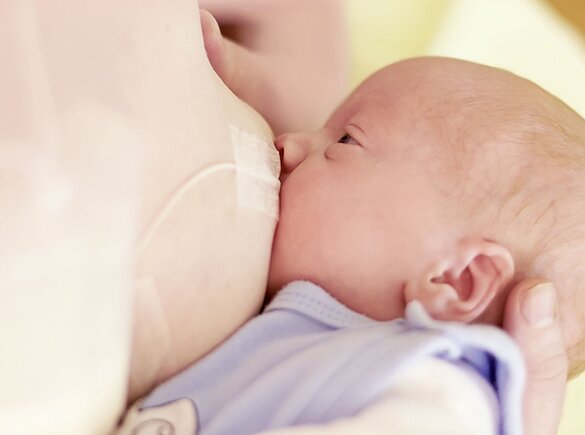 Een moeder die haar baby borstvoeding geeft en de voeding aanvult met het Medela Supplemental Nursing System™ (SNS).