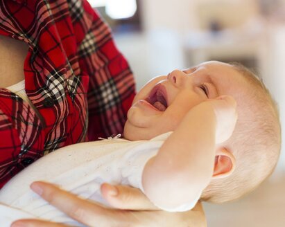 Ein Baby weint in den Armen seiner Mutter, während sie versucht, es zu stillen.