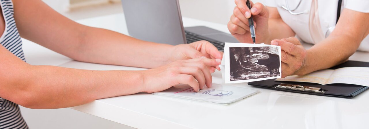 Eine schwangere Frau trifft sich mit einer medizinischen Fachkraft und hält ein Bild ihrer Ultraschalluntersuchung in der Hand.