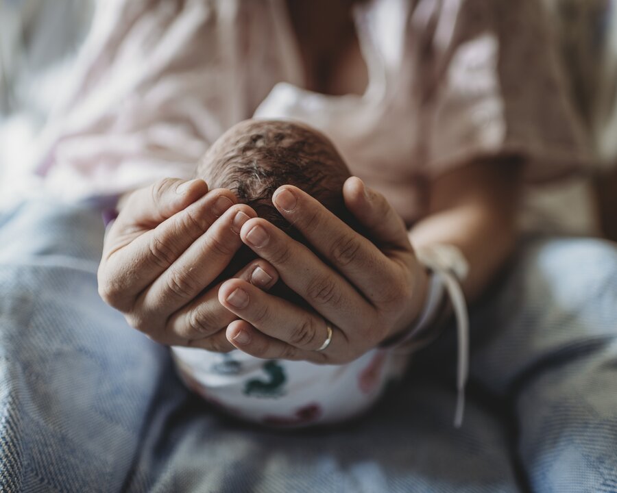 Een moeder wiegt het hoofdje van haar pasgeboren baby in haar handen terwijl ze in het ziekenhuis ligt.