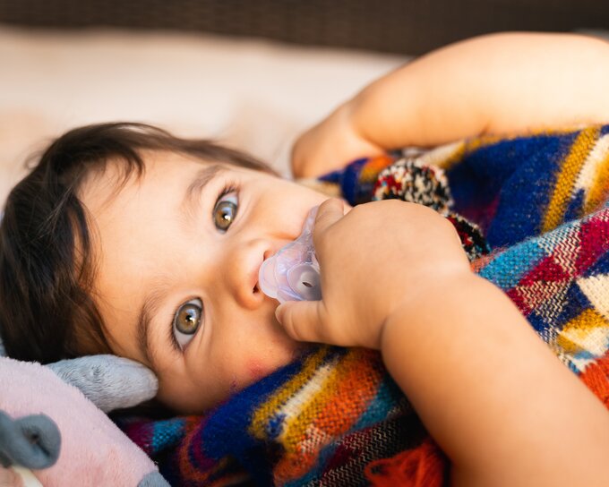 Un bambino sdraiato con una coperta e il suo ciuccio Medela SOFT SILICONE.