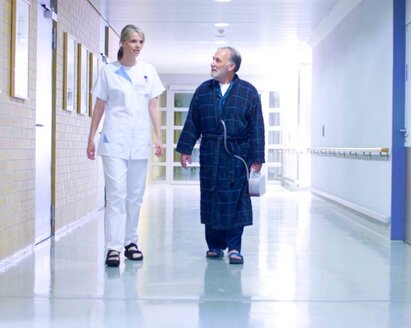 A doctor and a patient walk down a hospital corridor.